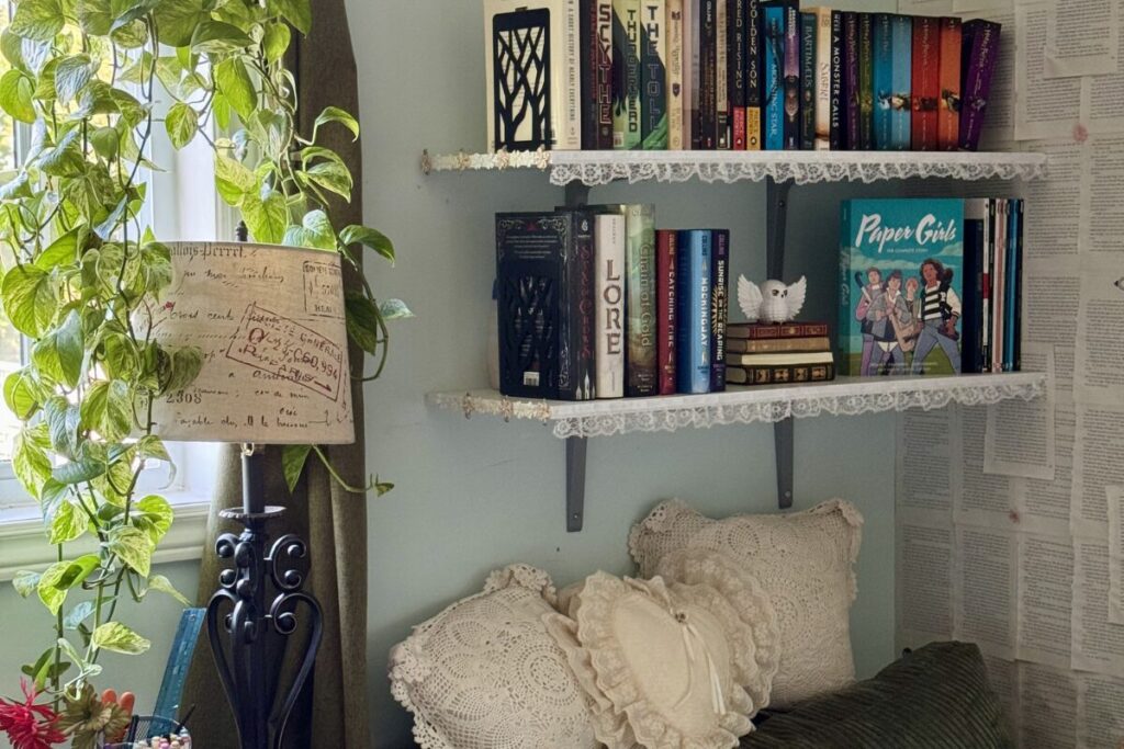 My reading nook A reading nook with two floating shelves packed with books, a hanging plant and a large green corner chair.